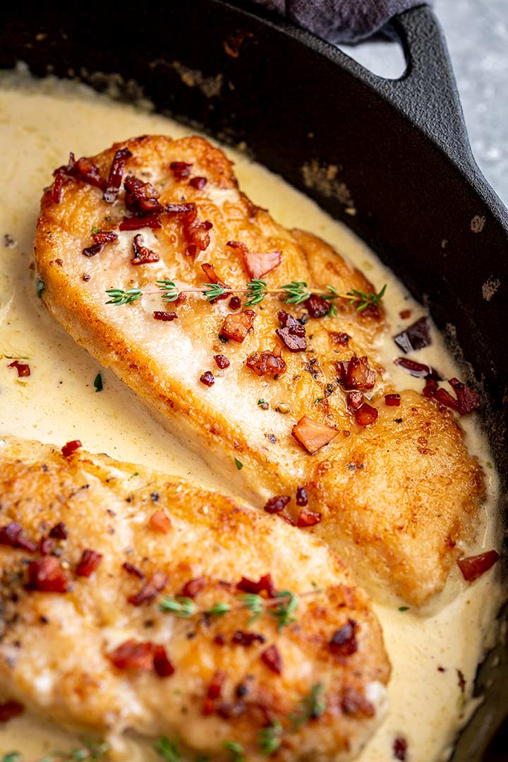 a chicken breast with bacon and thyme garnish in a pan of creamy sauce
