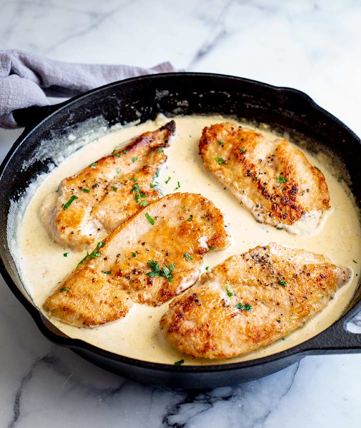 a cast iron pan of creamy chicken on a marble table
