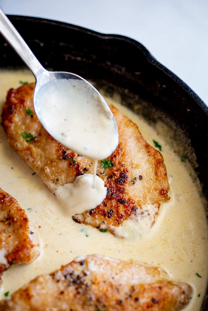 a spoon drizzling sauce over a cooked chicken breast
