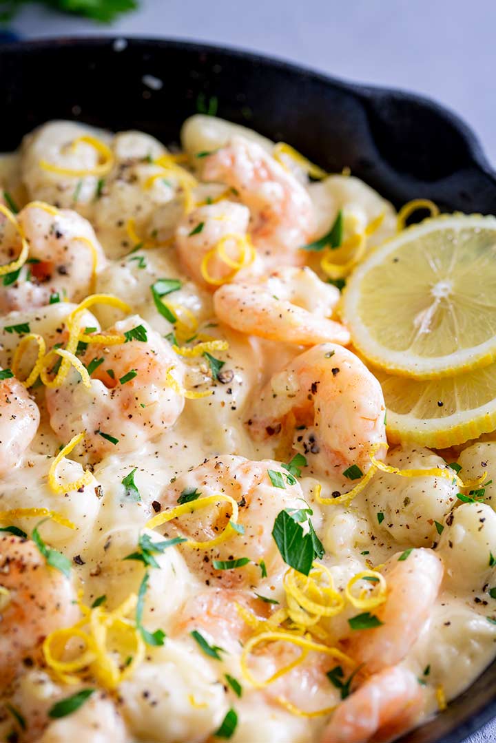 a skillet filled with creamy gnocchi and shrimp with lemon slices