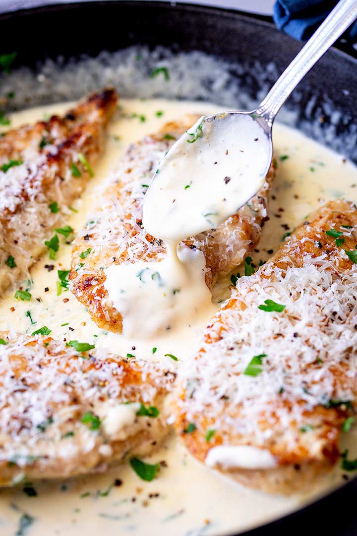 a spoon drizzling creamy sauce over a cooked chicken breast