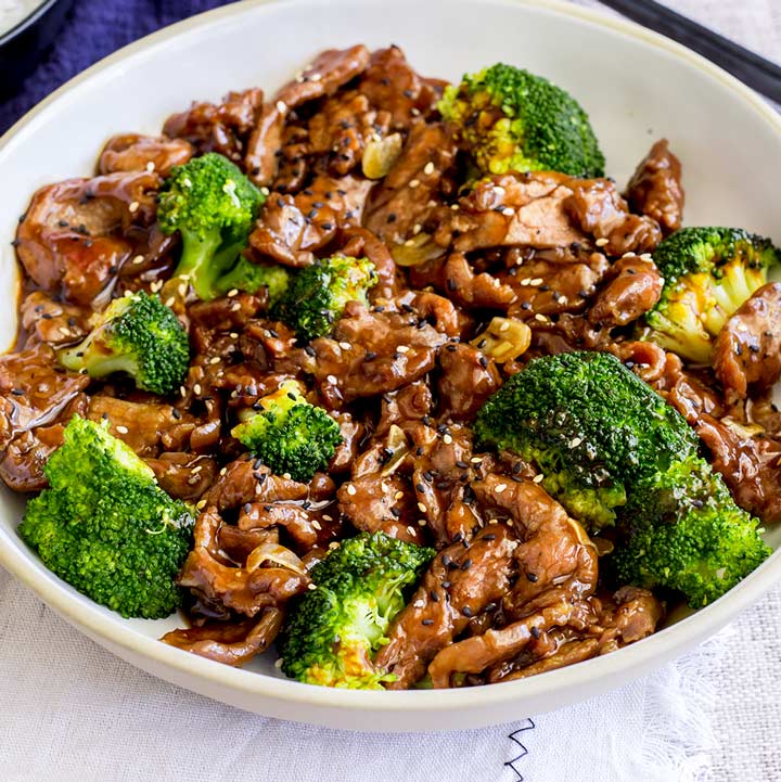 cream bowl of beef and broccoli stir fry with a blue napkin