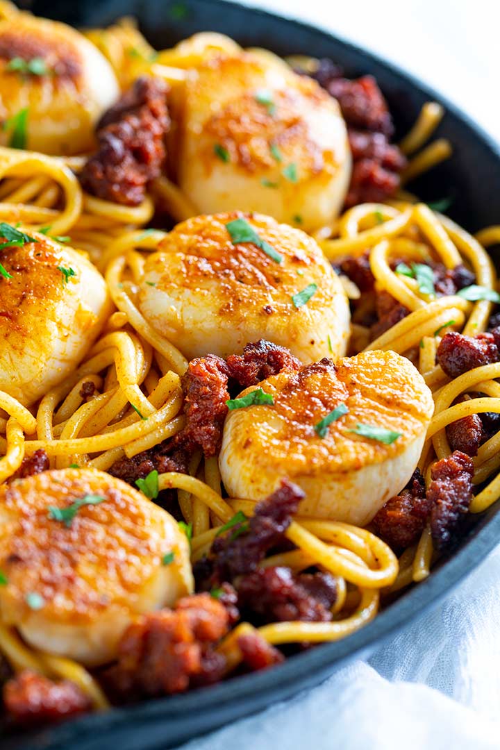 a cast iron skillet with chorizo spaghetti in it and seared scallops on top
