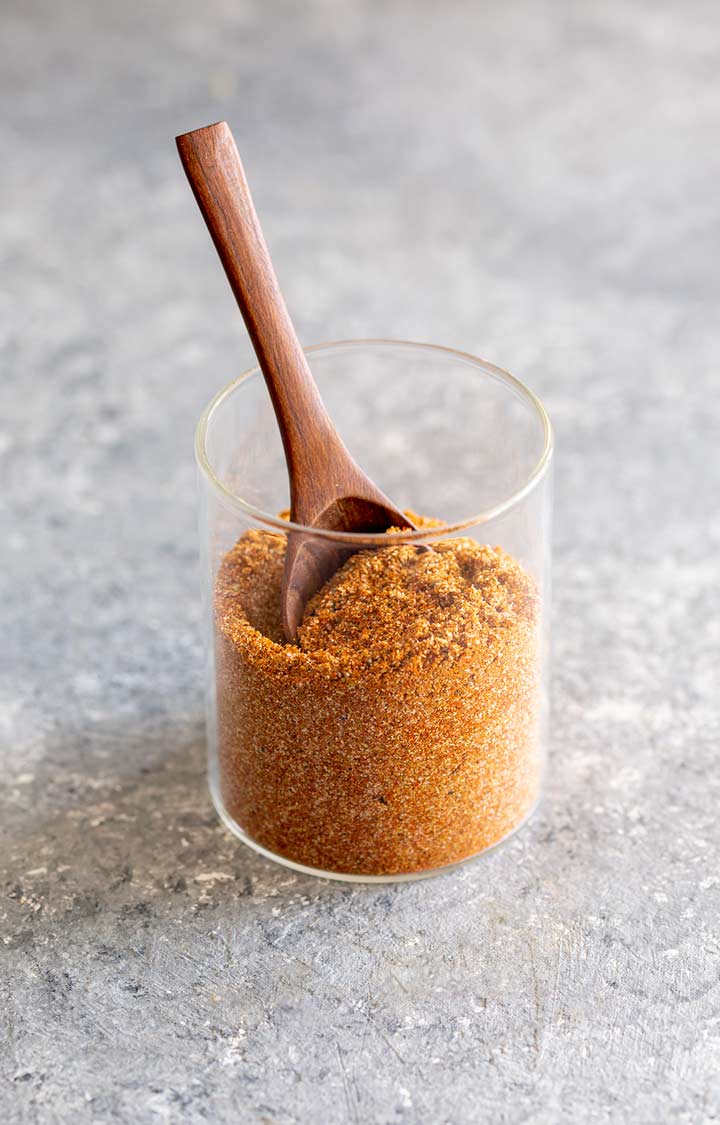 a glass jar of taco seasoning with a. wooden spoon in it