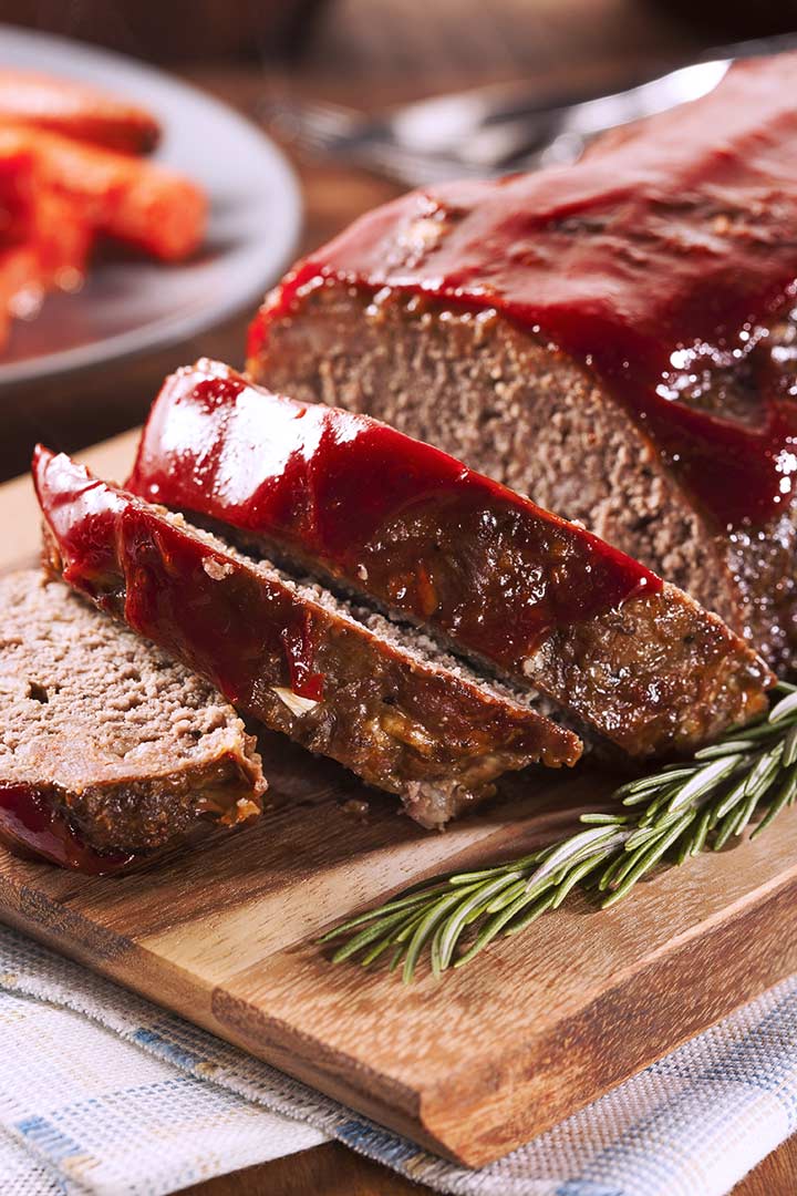 A Sliced meatloaf on a wooden board with rosemary garnish