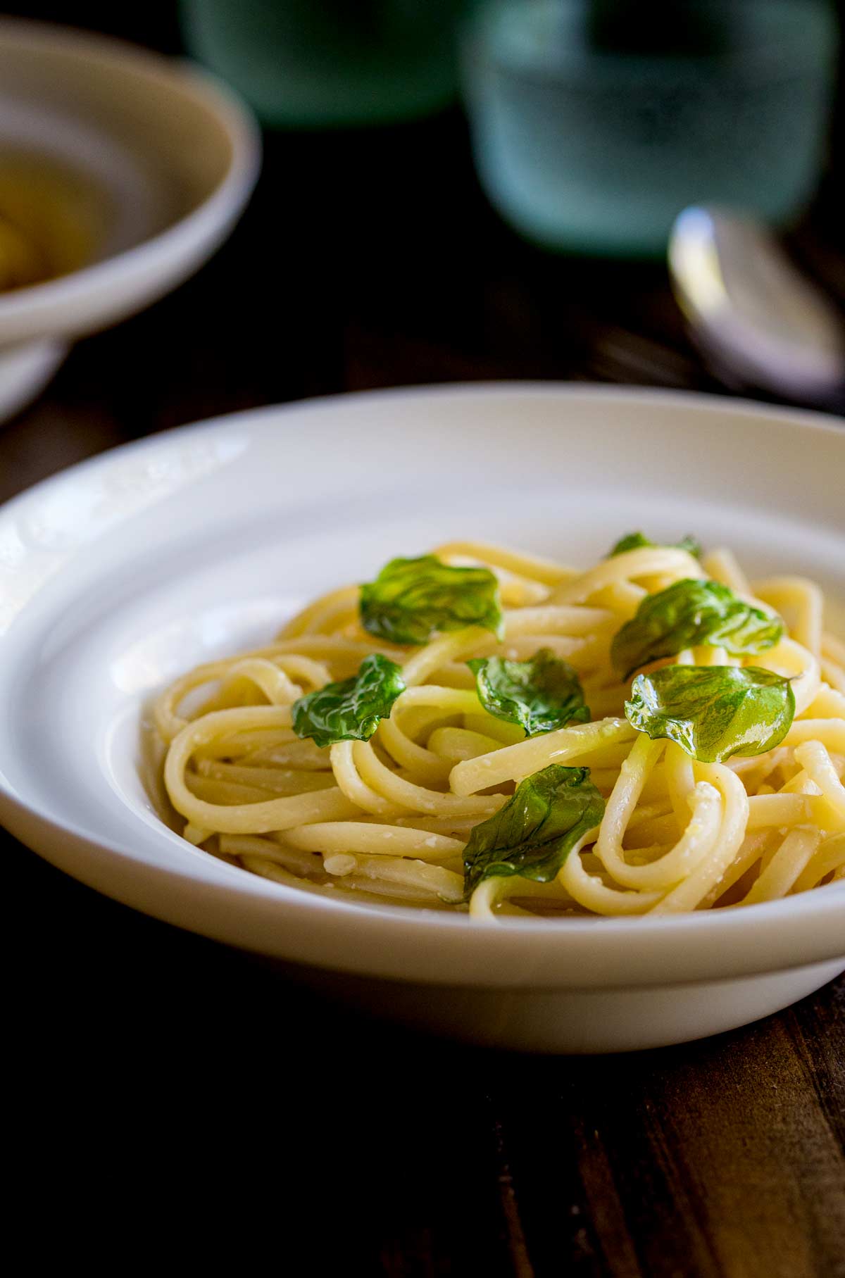 a white bowl on a dark table filled with pasta and garnished with basil leaves