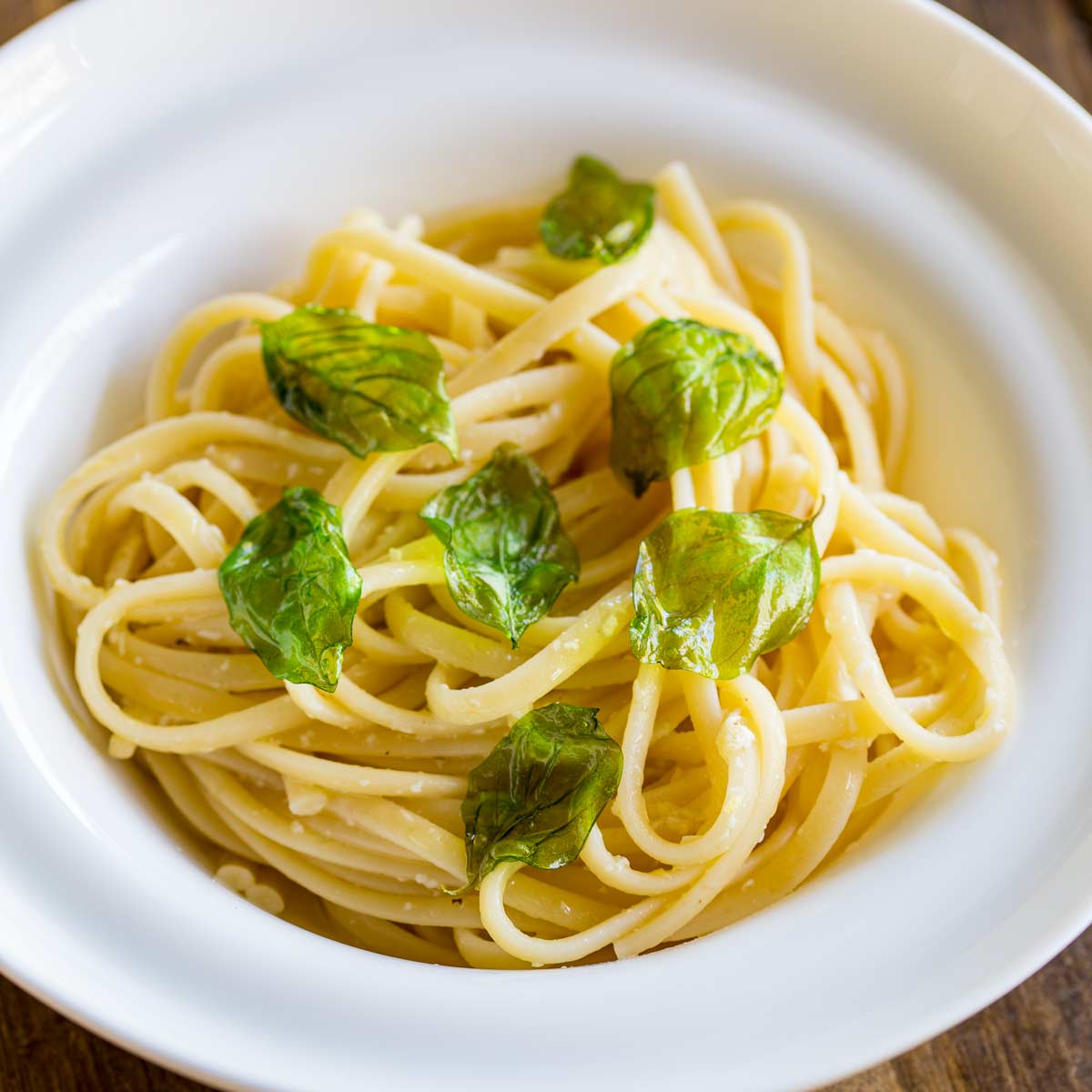 close up on some lemon pasta in a white bowl garnished with basil
