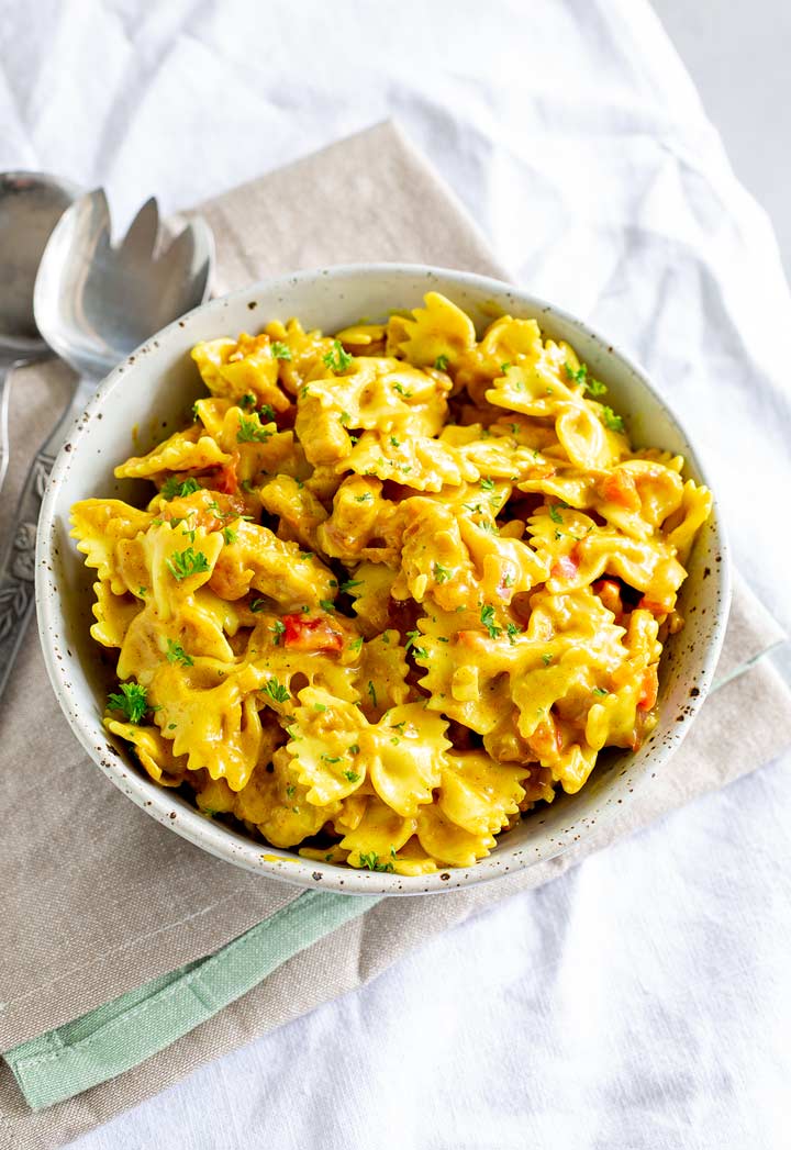 a rustic bowl filled with bowtie pasta in a yellow sauce on a white table