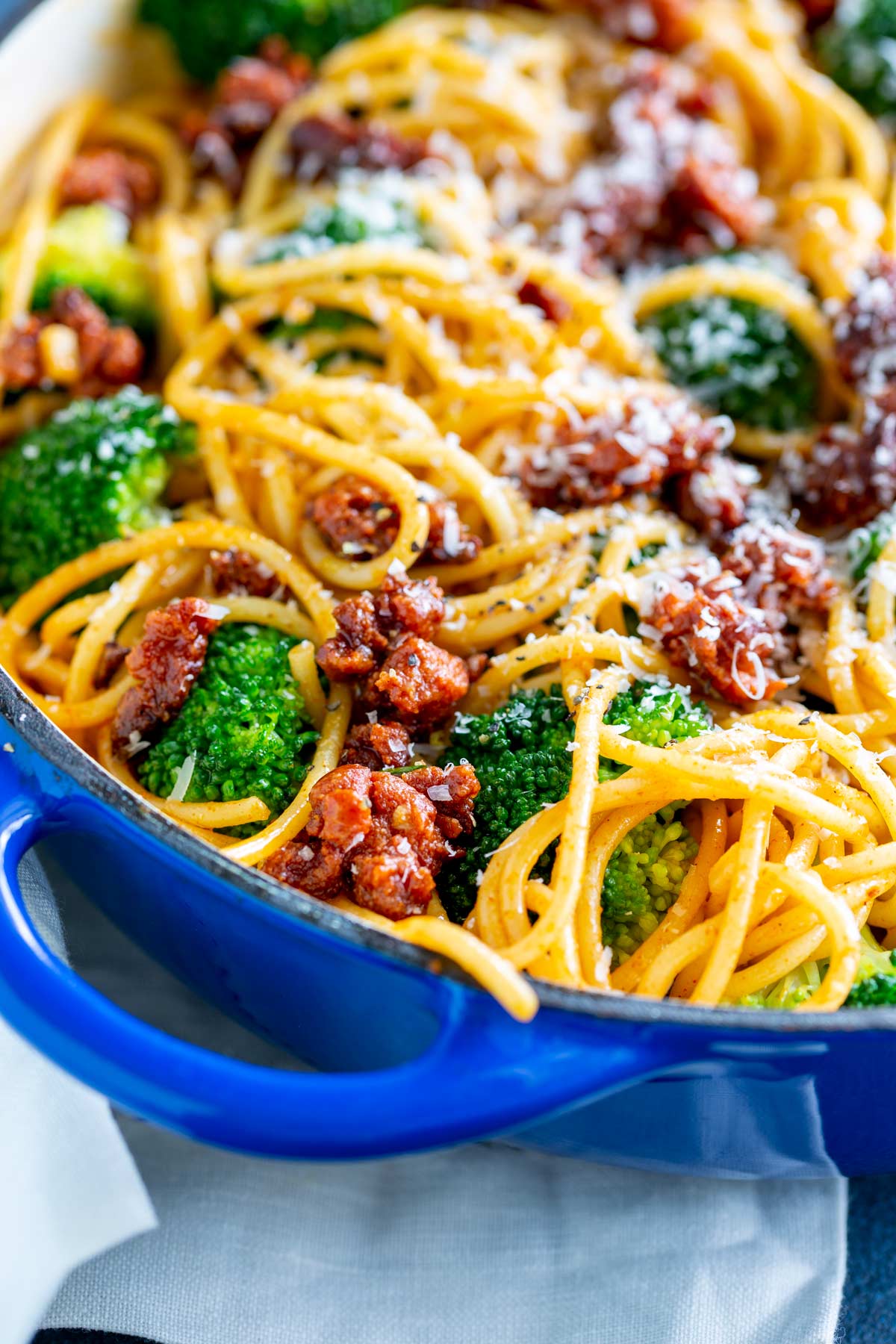 a blue dish filled with spaghetti, chorizo and broccoli