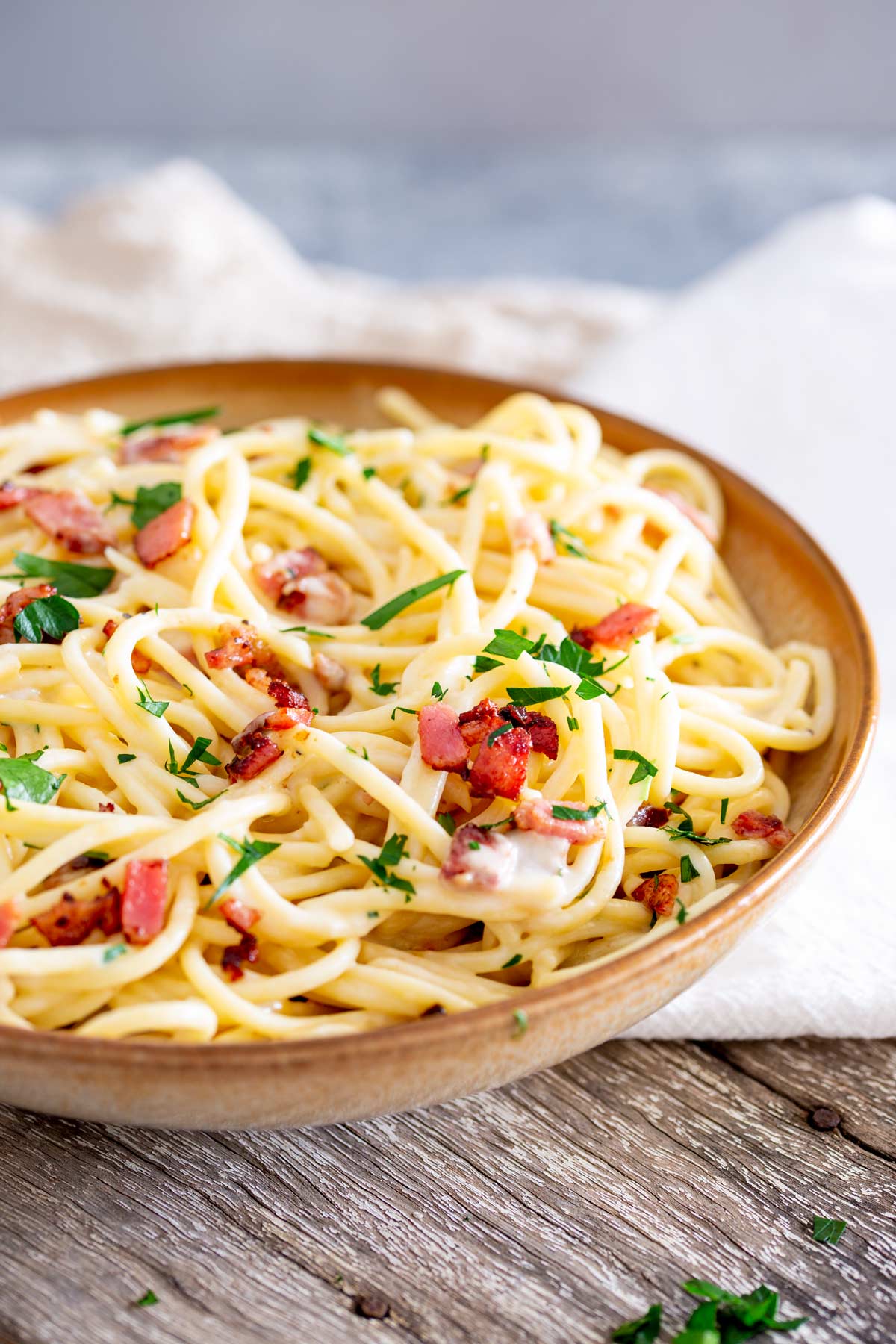 a bowl of creamy pasta with bacon on a wooden table with a white napkin