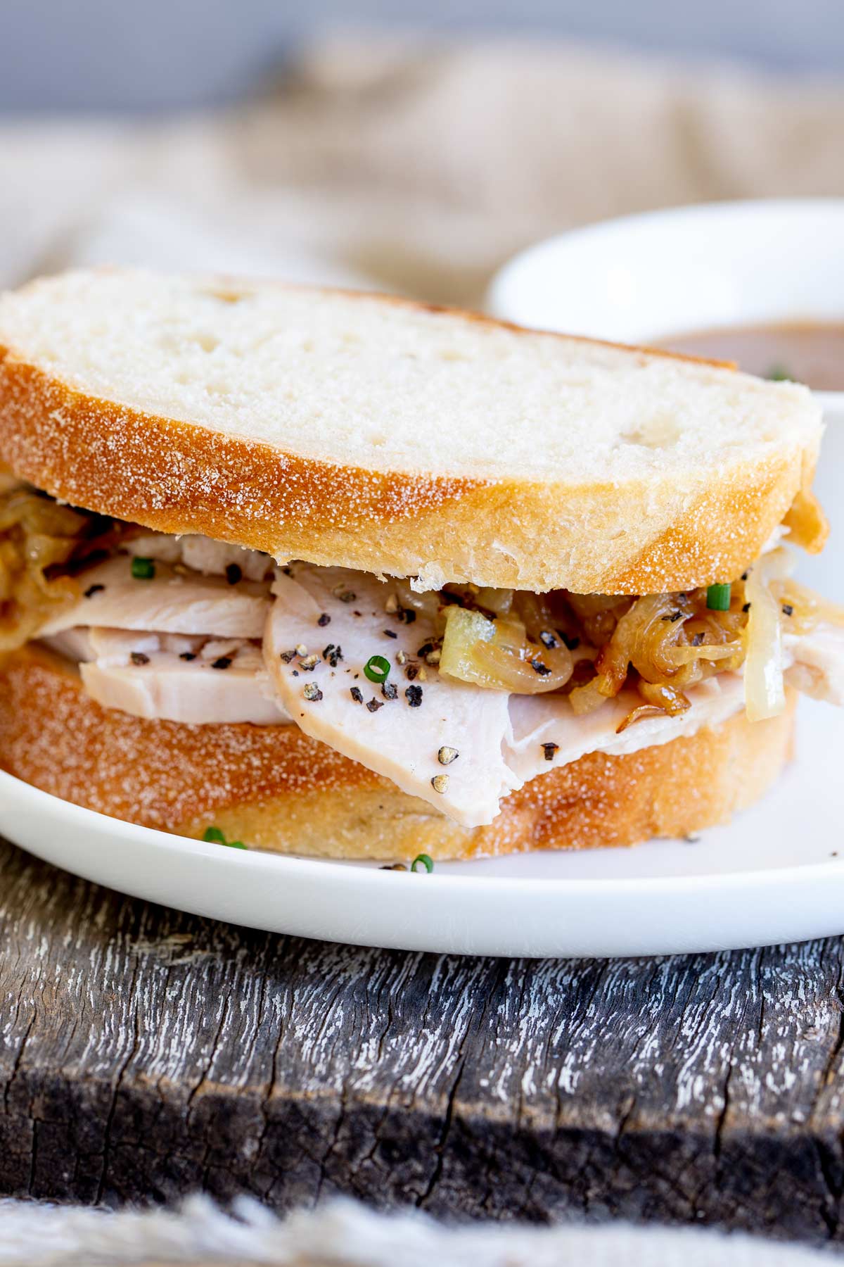 a turkey sandwich with onions on a white plate on a wooden board