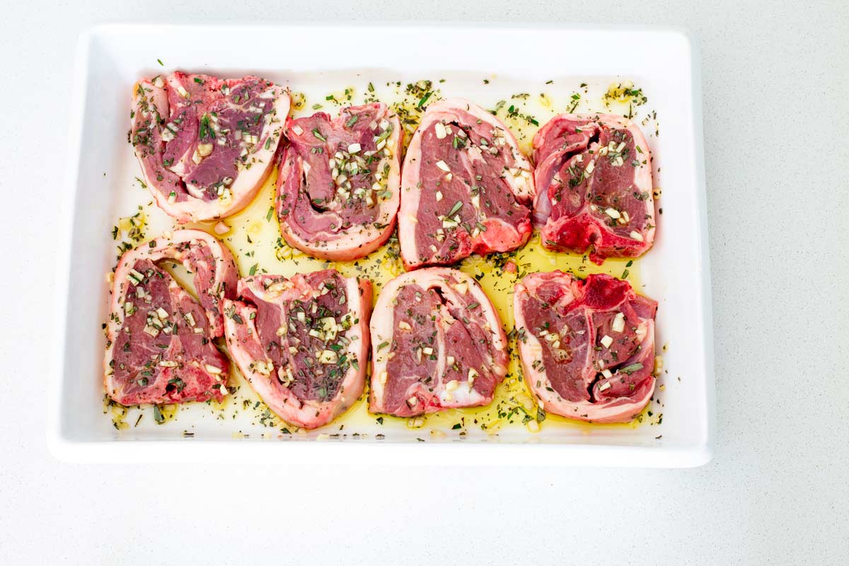 8 raw lamb chops marinating in a baking dish