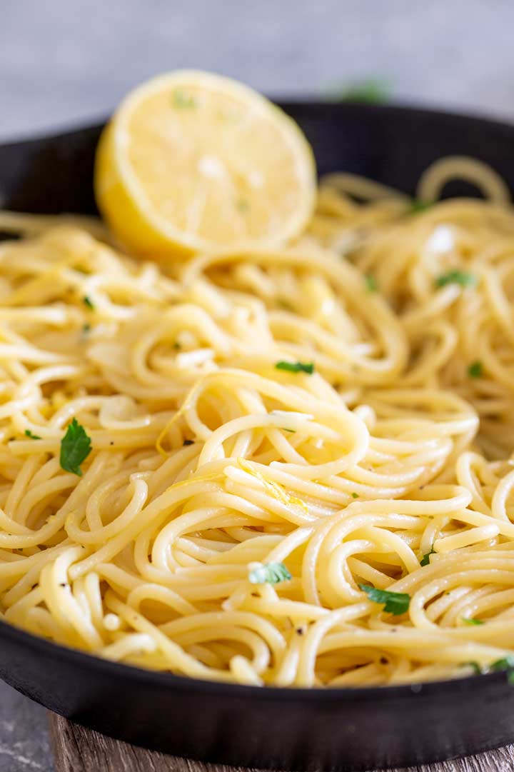 a skillet of pasta with a lemon wedge