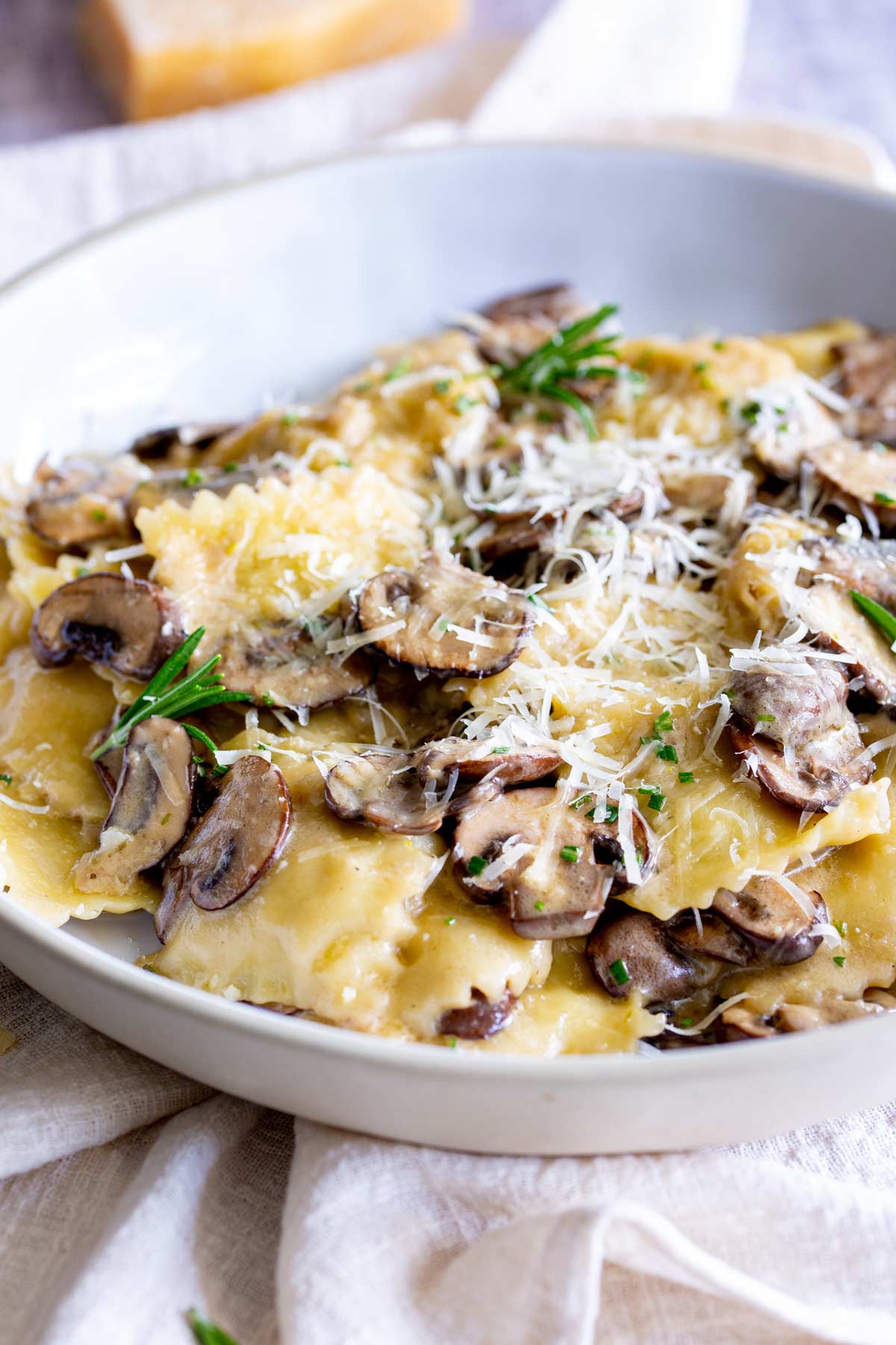 a white bowl of ravioli with mushrooms and parmesan