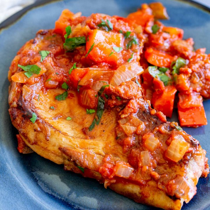 a pork chop on a blue plate, topped with tomato