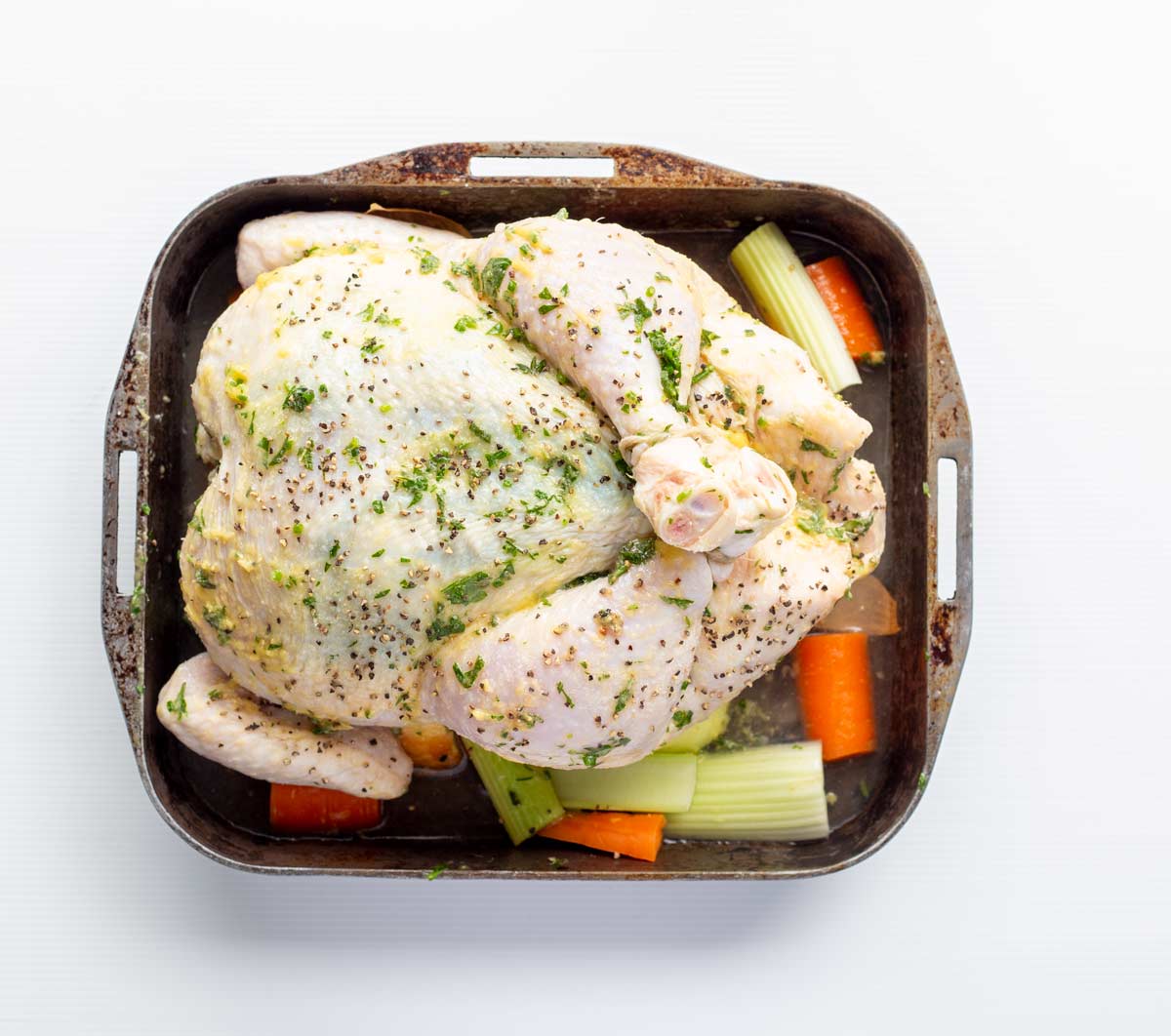 a raw chicken in a roasting dish with veg underneath