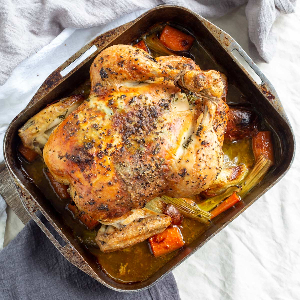 A trussed cooked roast chicken in a metal roasting dish