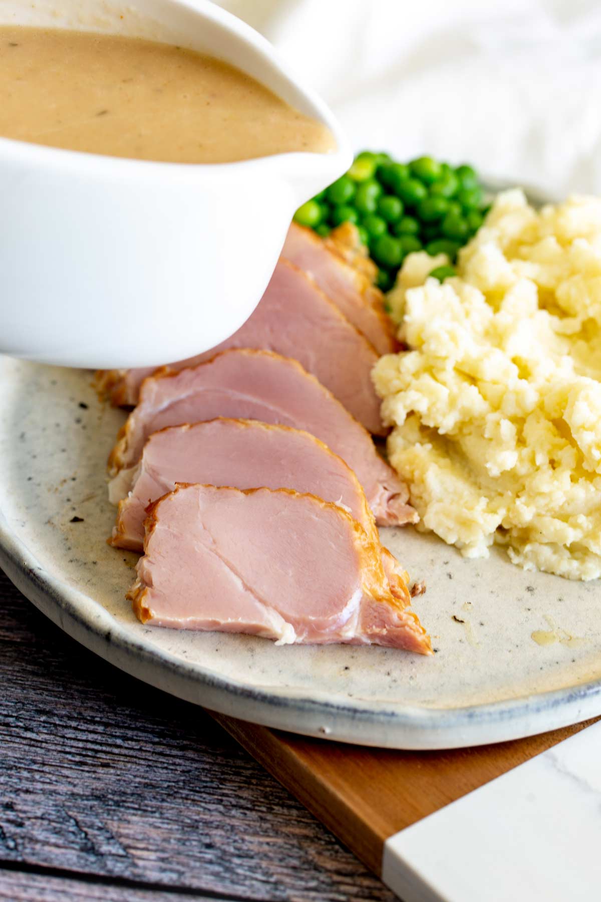 a gravy boat pouring gravy over ham and mashed potato