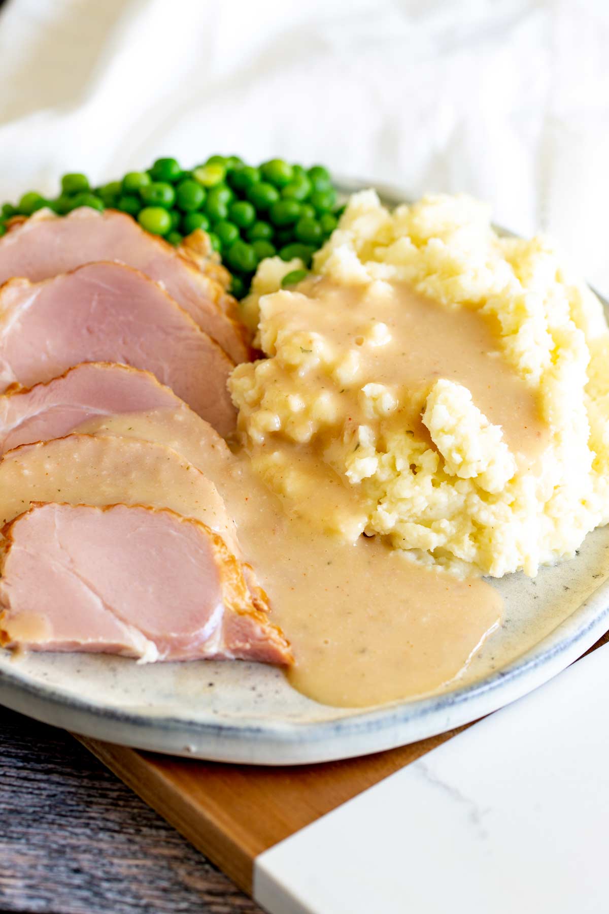 A stone plate with a creamy gravy poured over slices of ham and mashed potato