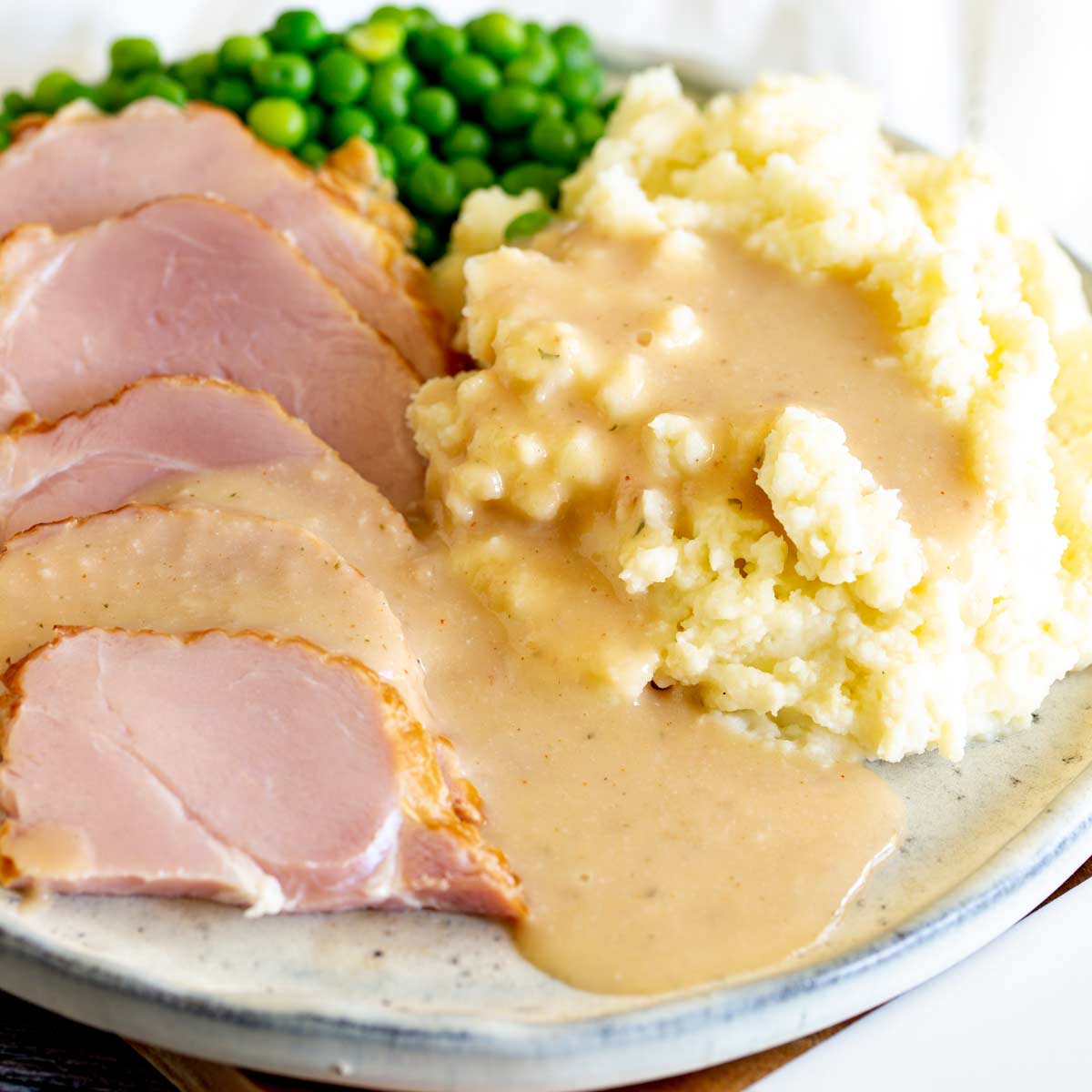 ham, mashed potato, peas and gravy on a stone plate