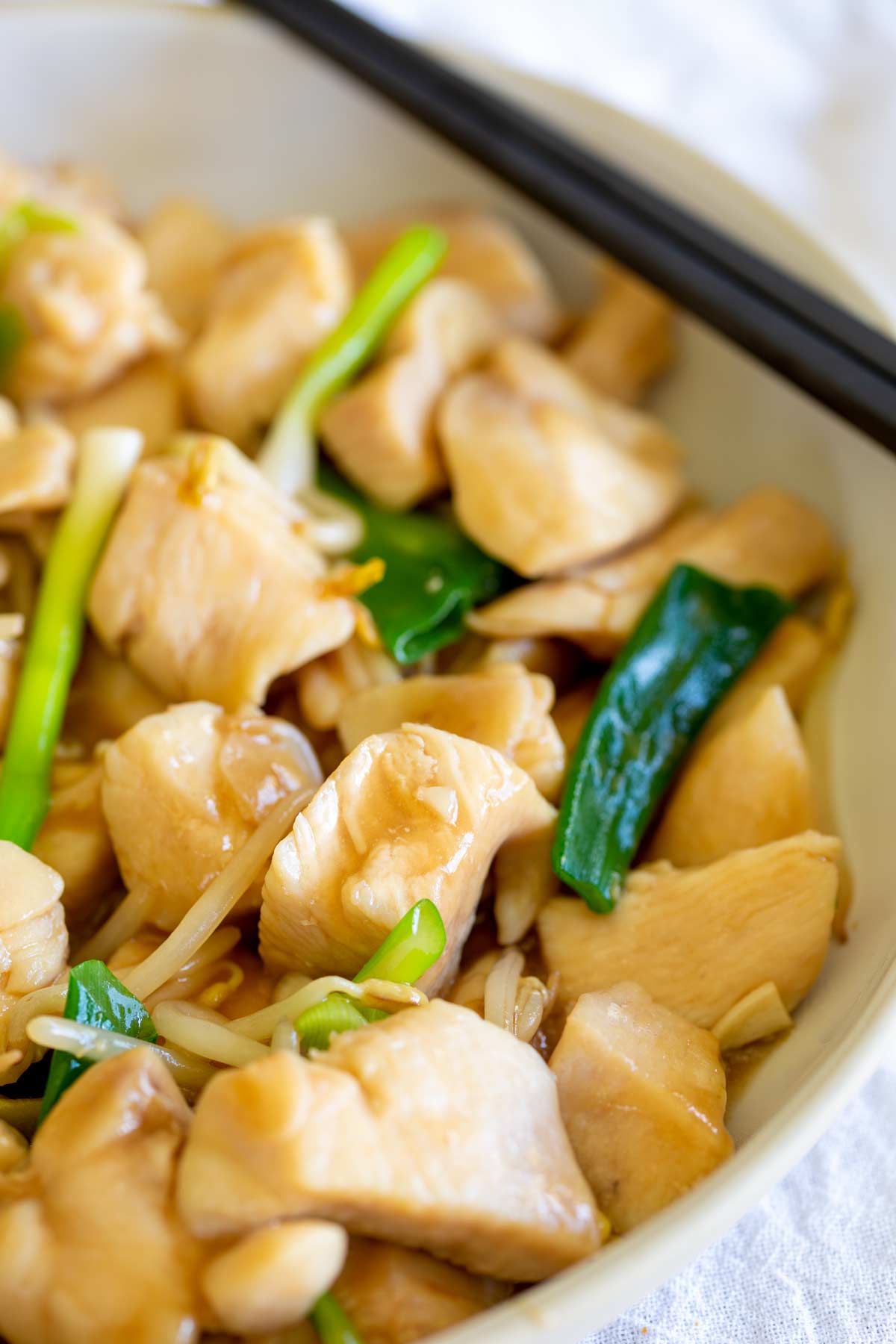 Chicken, garlic beansprouts and green onions in a white bowl with garlic sauce