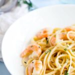 shrimp pasta in a white bowl with rosemary behind