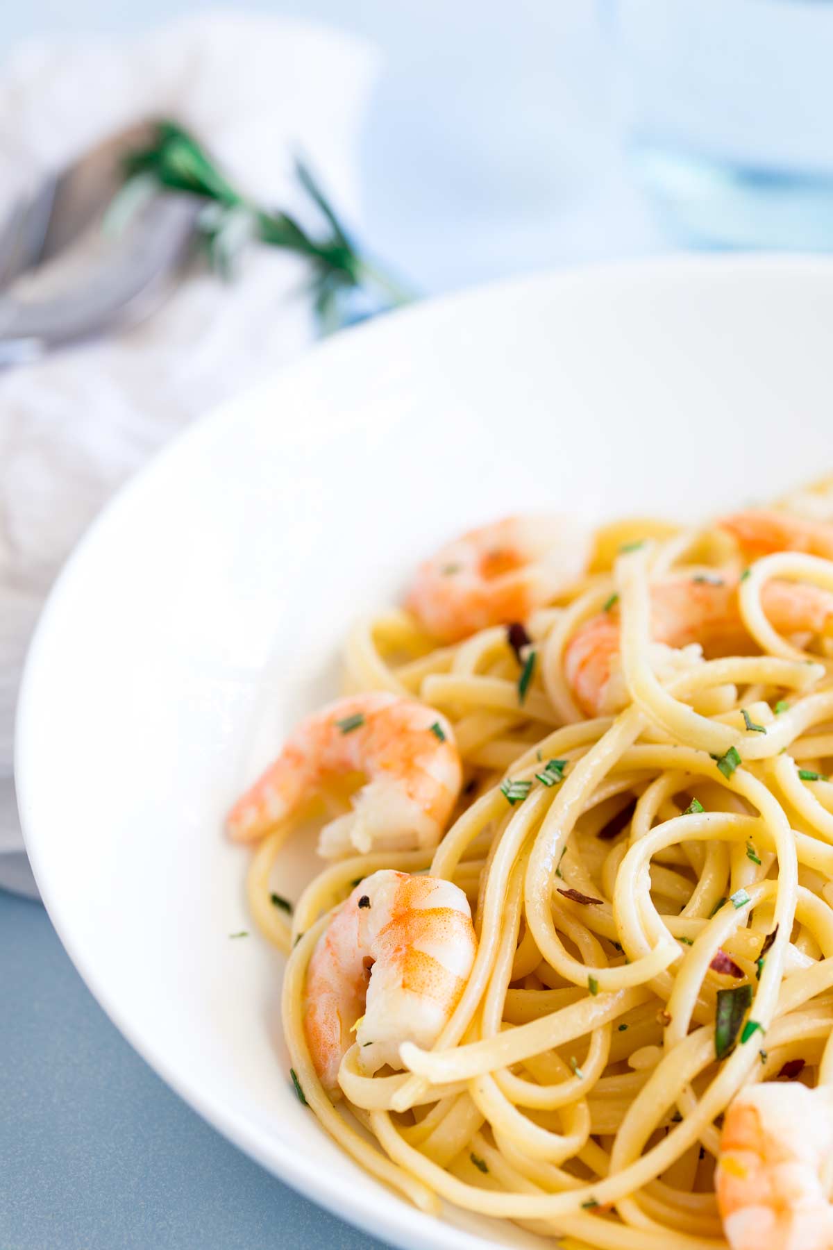 shrimp pasta in a white bowl with rosemary behind