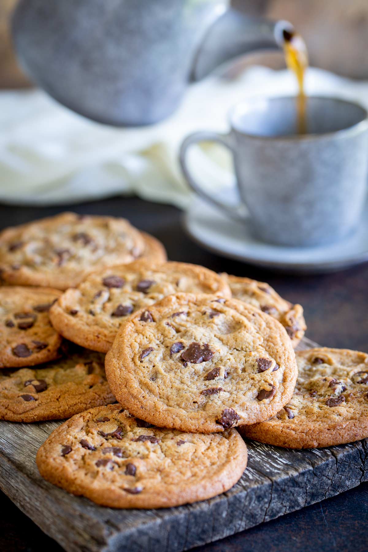 choc chip cookies on a wooden board with a teapot behind