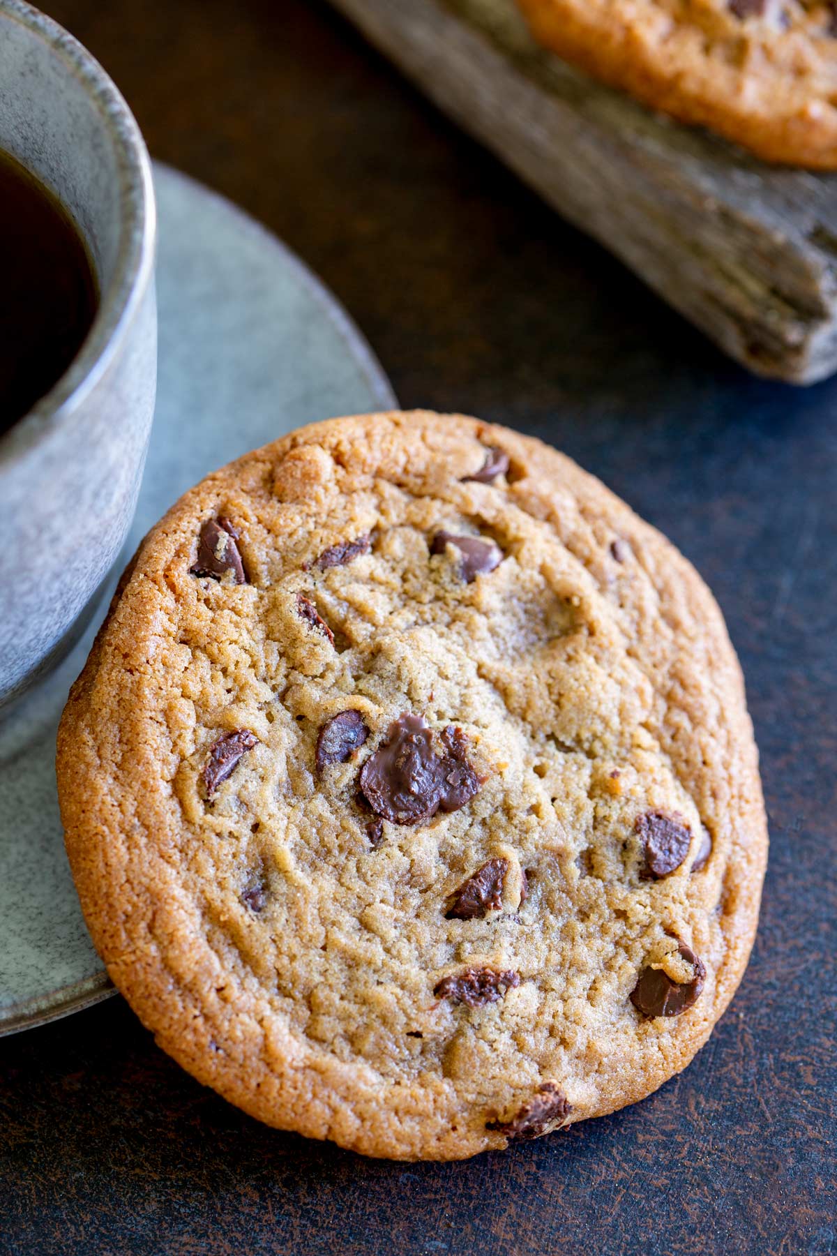 a subway style choc chip cookie leaning against a cup