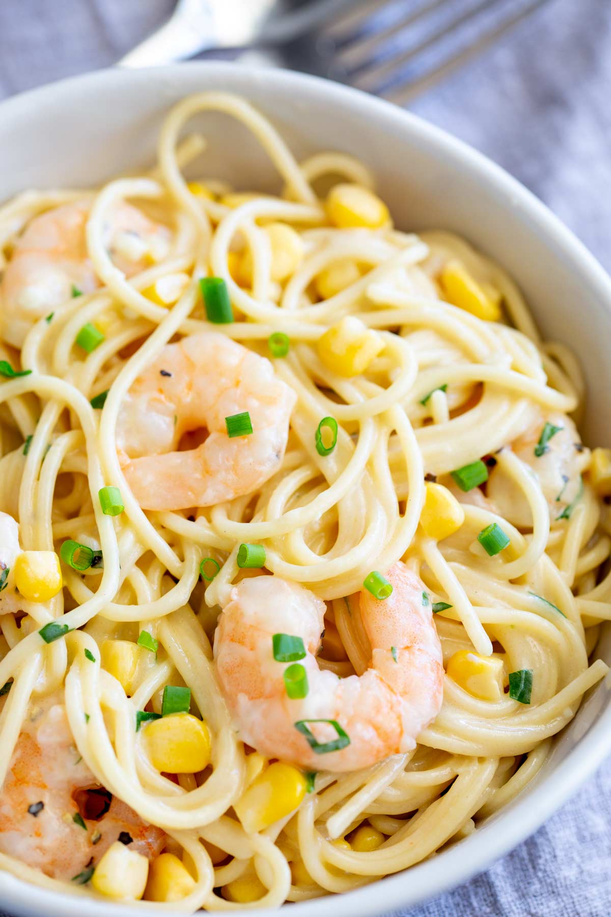corn and shrimp pasta garnished with chives in a white bowl