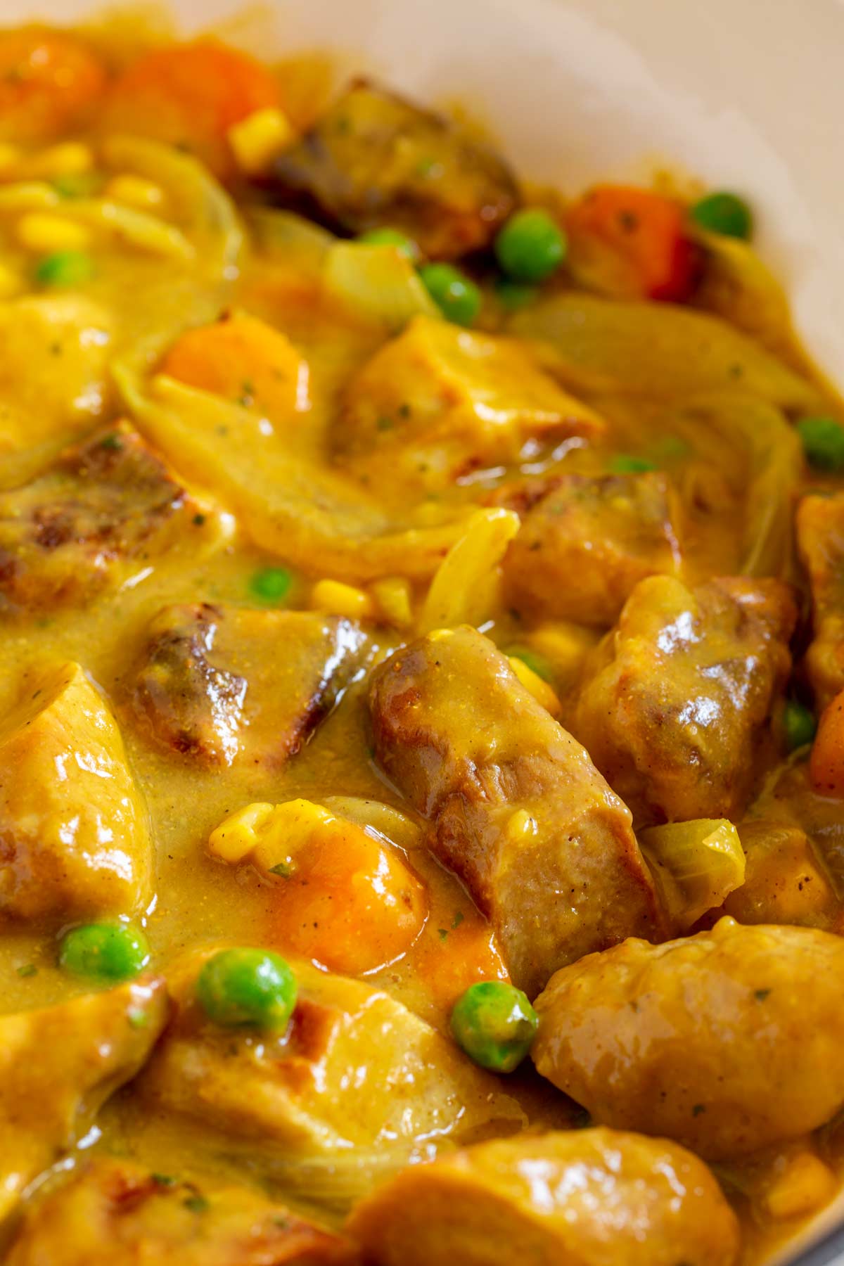 chunks of sausage in a curry sauce with carrots pea and corn