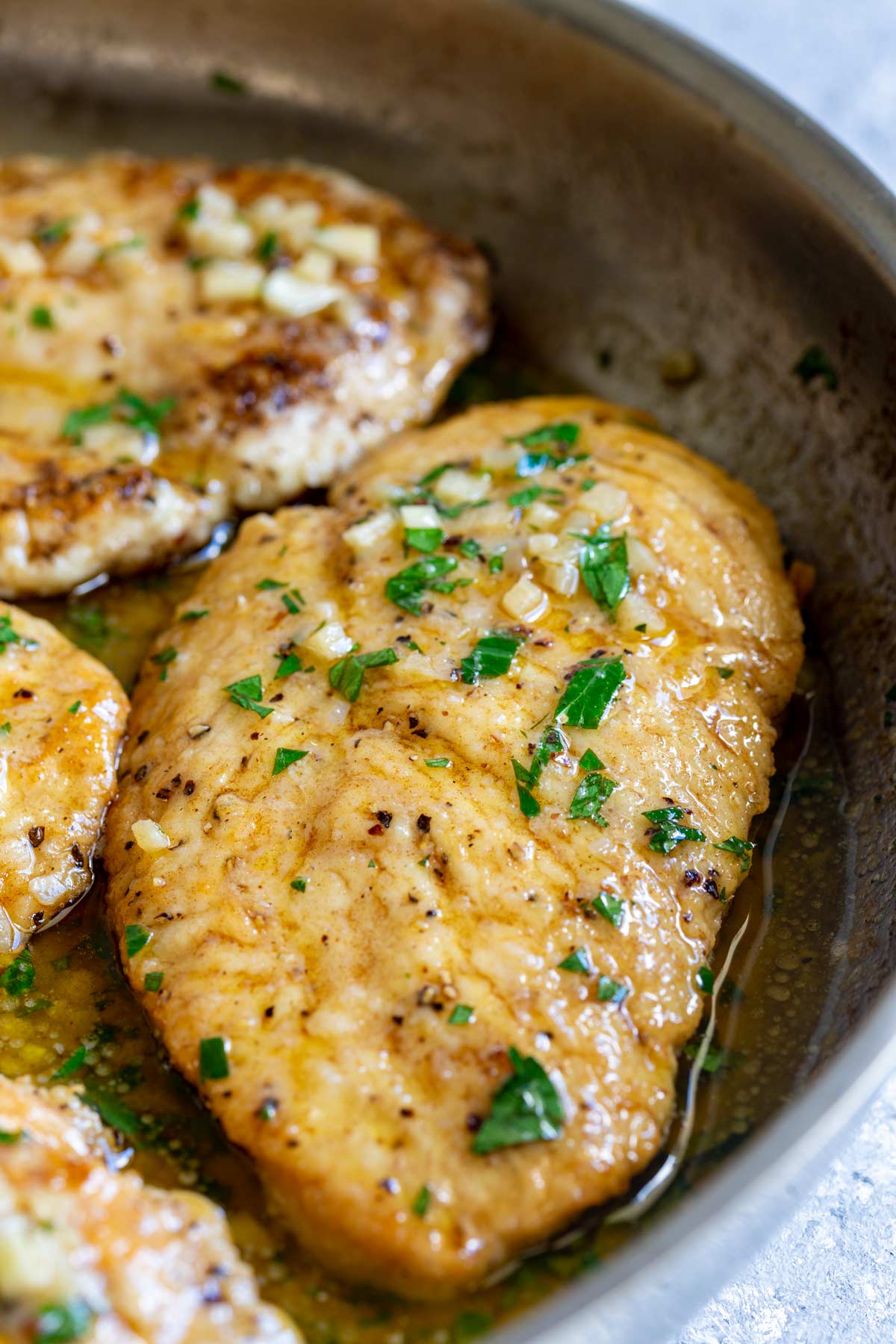 a panfried chicken breast in a skillet with garlic and chopped parsley