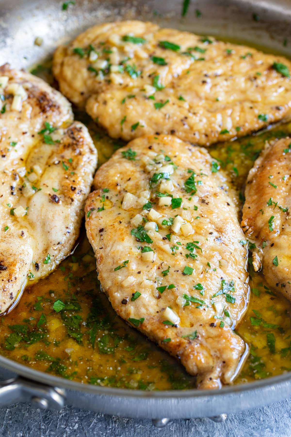 4 chicken breasts in a metal skillet with garlic butter