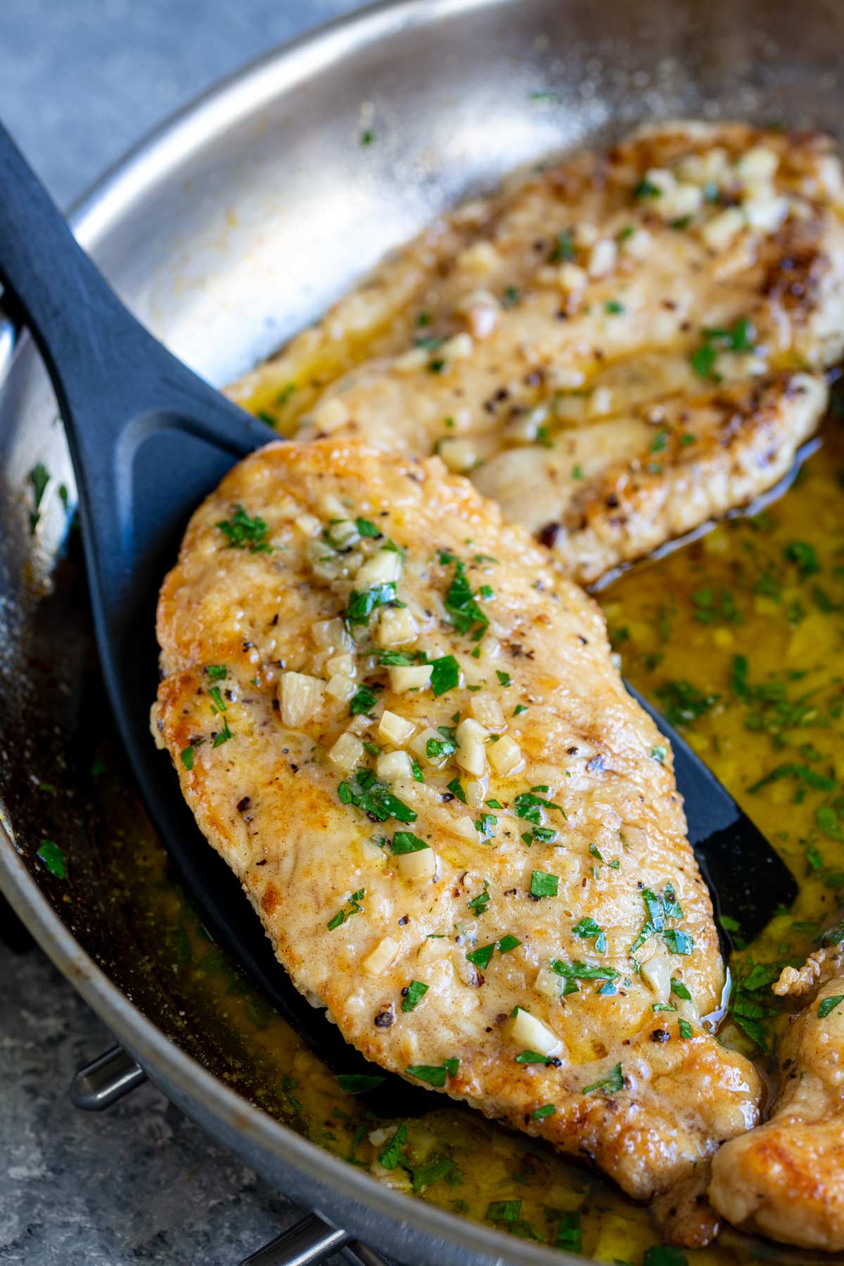 A garlic chicken breast being lifted from skillet with a black spatula