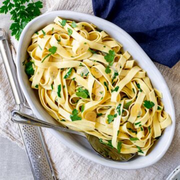 overhead shot of an oval dish of tagliatelle with parsley and garlic mixed through