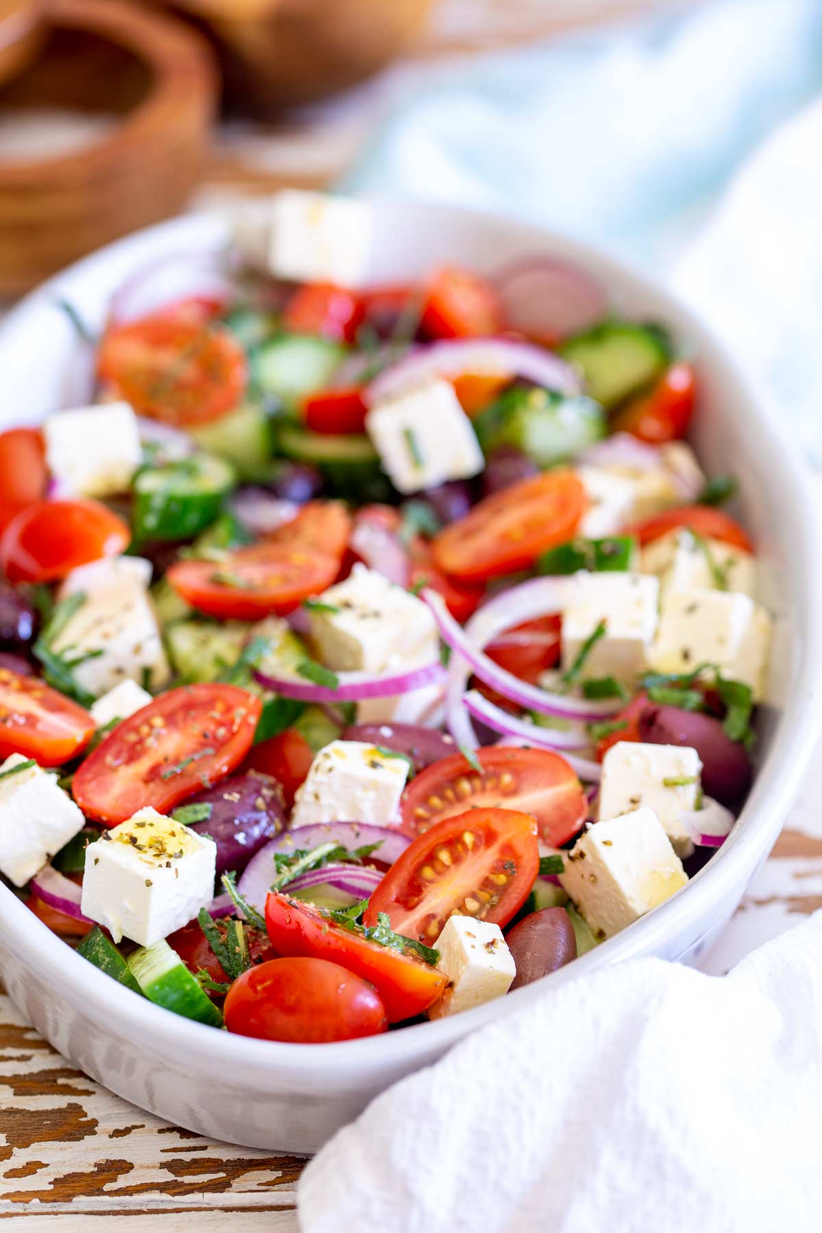 an oval dish of salad on a wooden table with cubed feta and cherry tomatoes