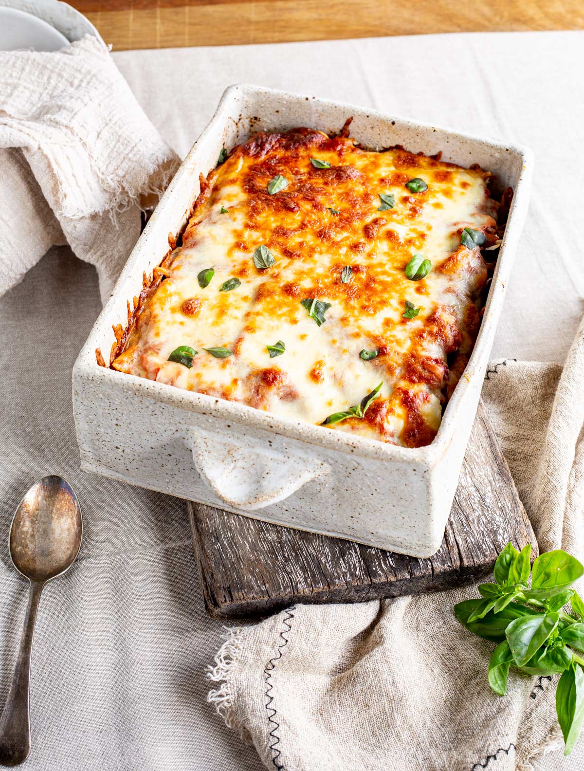 a large serving dish filled with baked pasta with basil leaves on top