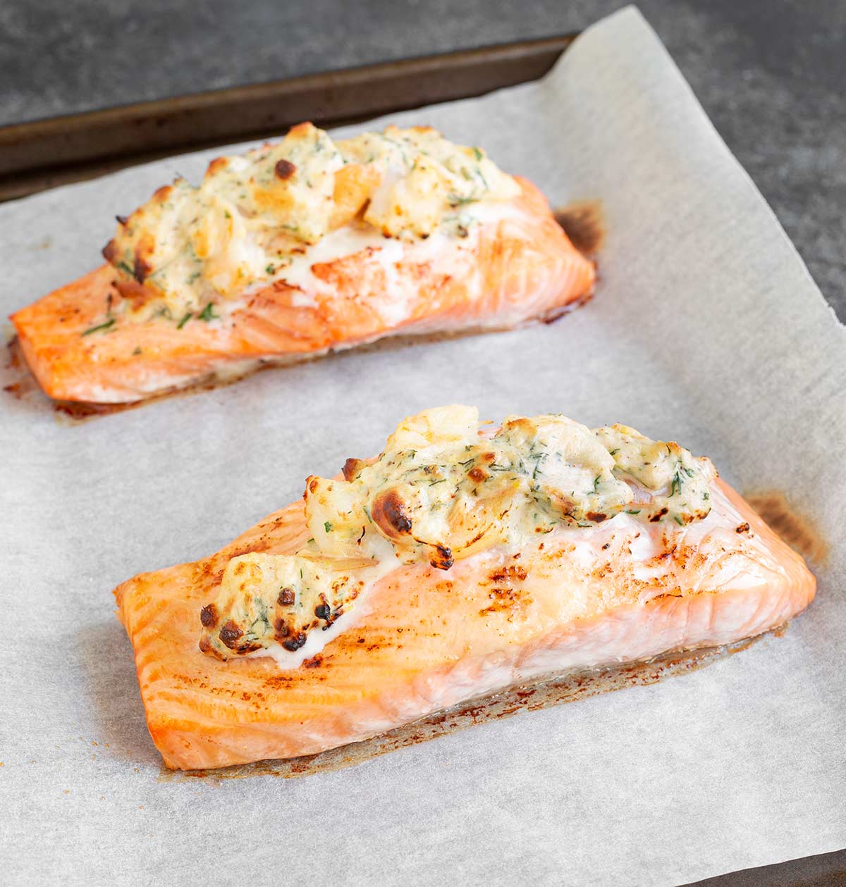 two cooked stuffed salmon fillets on a baking tray lined with parchment