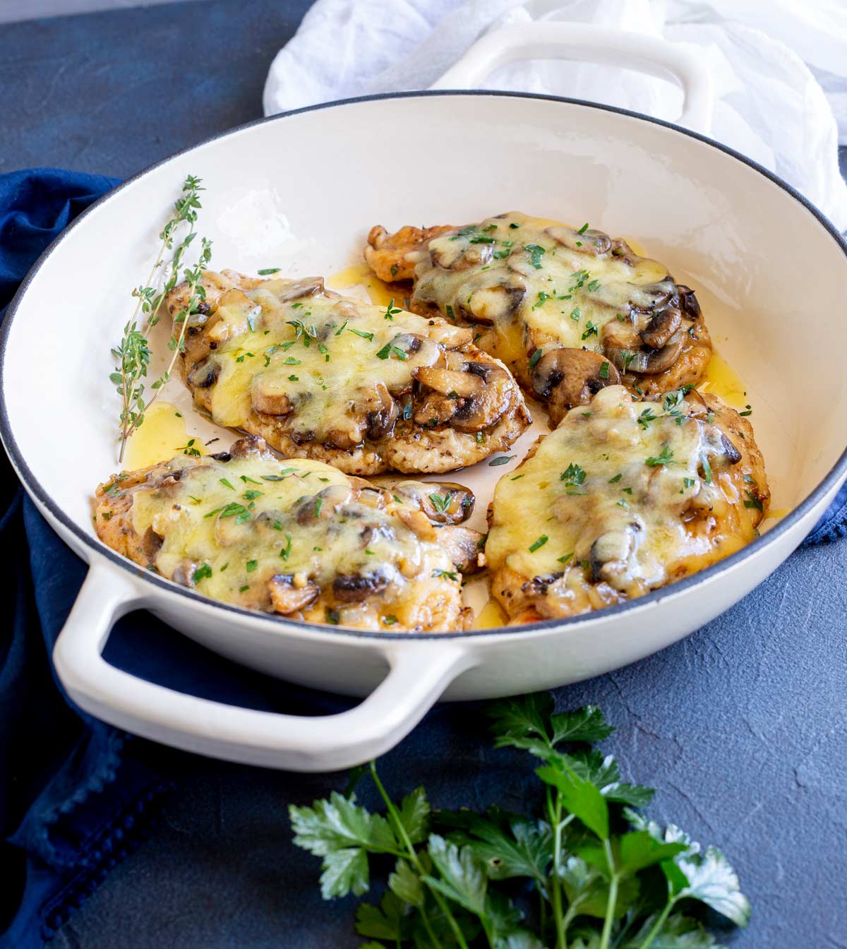 4 chicken breast fillets with mushrooms and cheese in a dish on a blue table