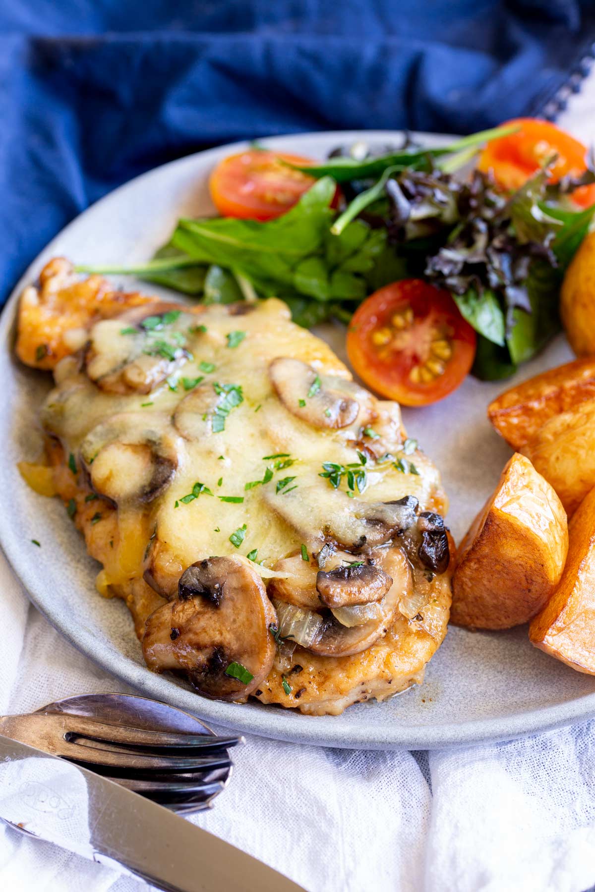 a chicken breast with mushrooms and cheese on a plate with salad and potatoes