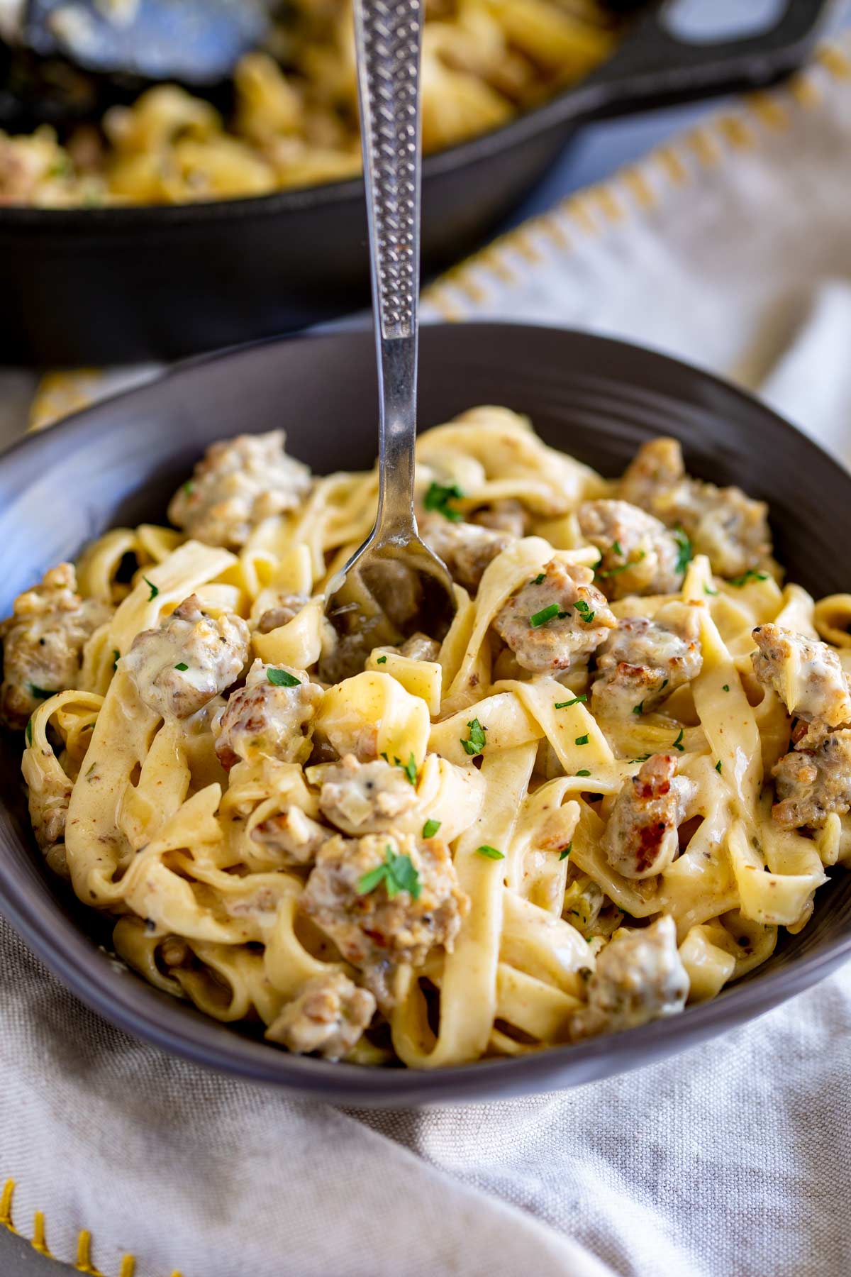 a fork standing in a bowl of crumbled sausage and tagliatelle