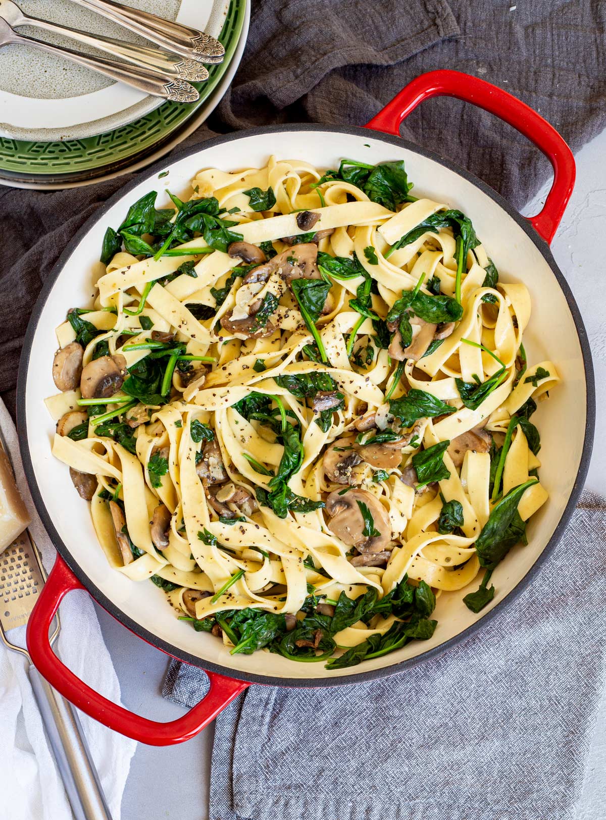 overhead shot of a red cast iron pan with fettuccine mushrooms and spinach in it