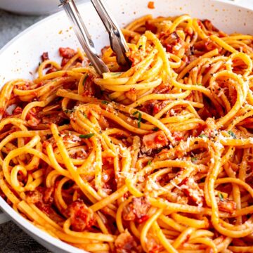 close up on a pair of tongs swirling tomato bacon pasta up
