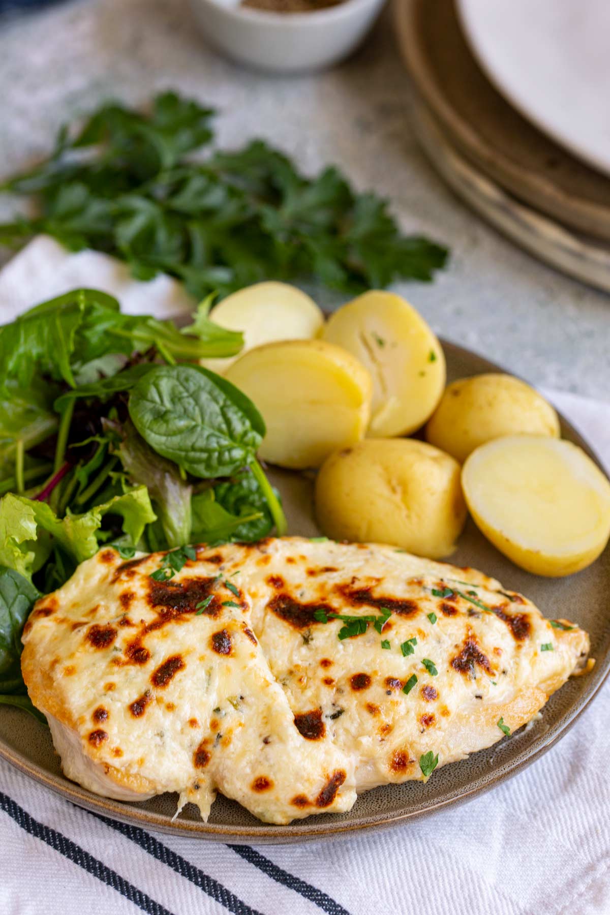 a chicken breast covered in a cheesy sauce on a plate with potatoes and salad