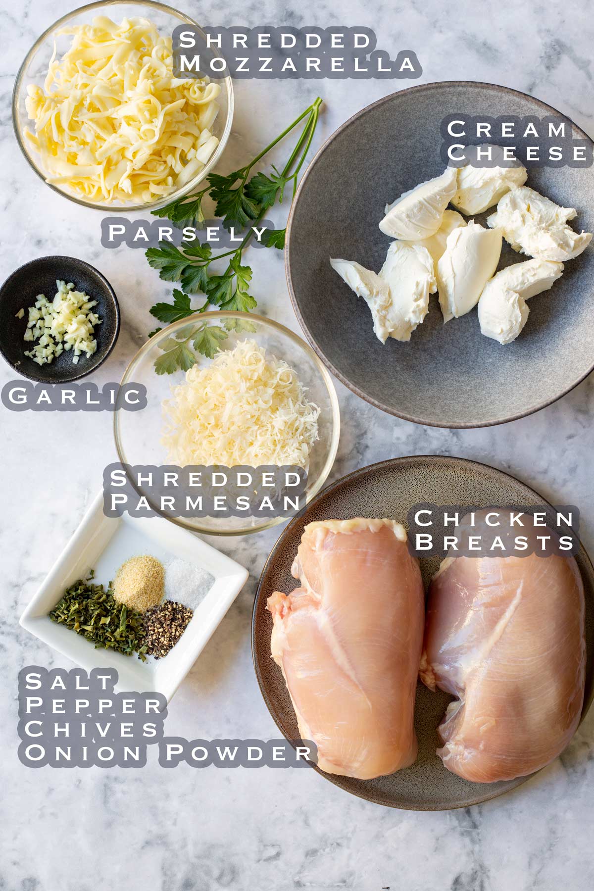 ingredients for cheesy chicken breasts laid out on a marble bench top