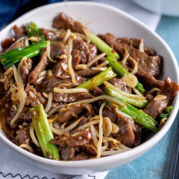 a white bowl of beef stir fry with bean shoots and green onions