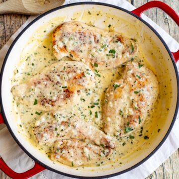 overhead shot of 4 chicken breasts in a cast iron skillet with a creamy sauce