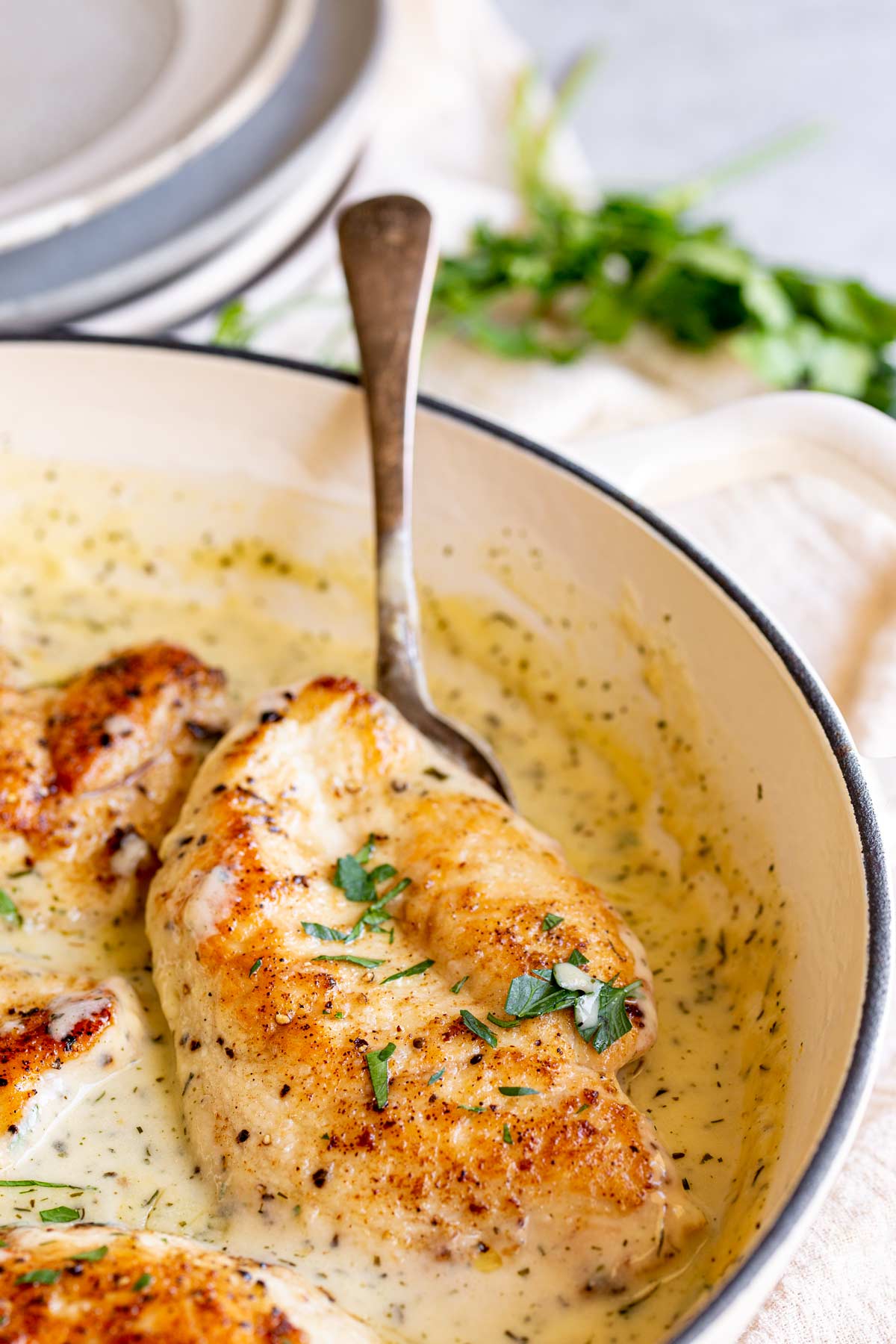 a spoon scooping up a chicken breast from a pan of creamy sauce