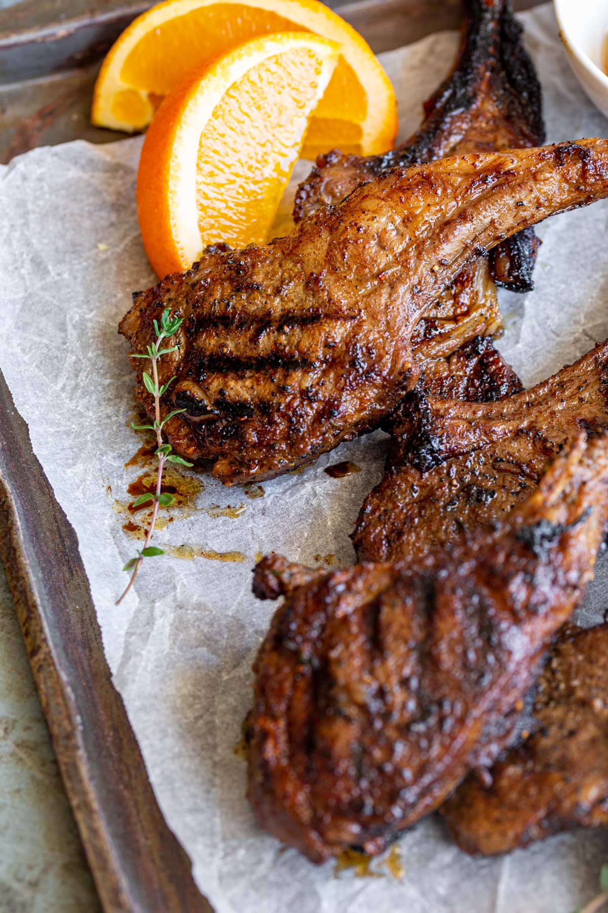 Honey Jerk lamb chops in a pile of a lined baking tray with wedges of orange