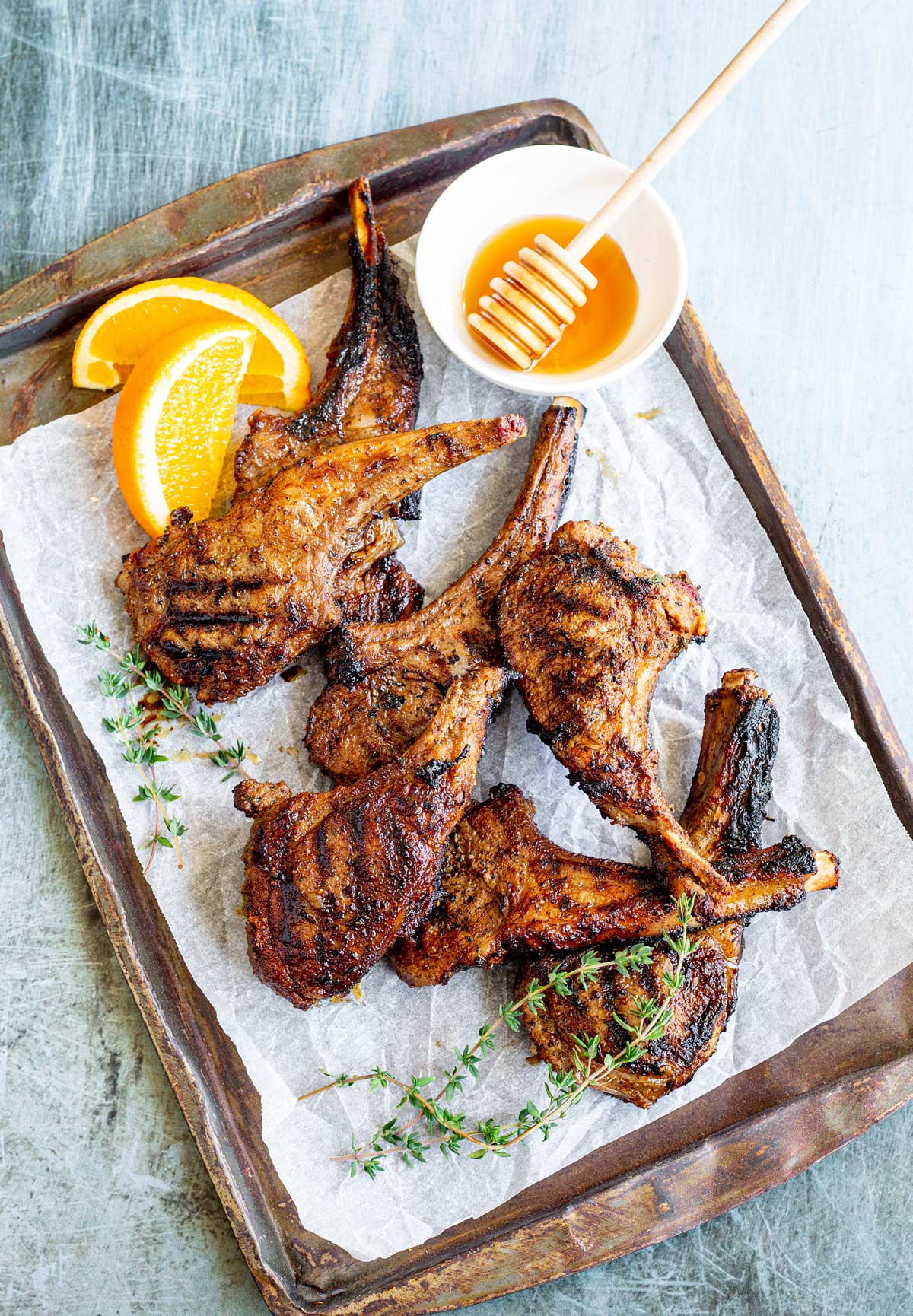 a tray of lamb chops on a scratched table with honey and oranges as garnish